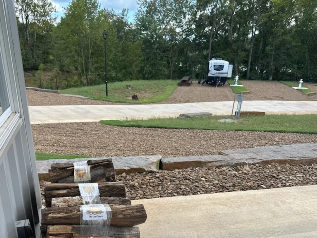 Bundled firewood at the vending barn with a travel trailer on a site across the loop