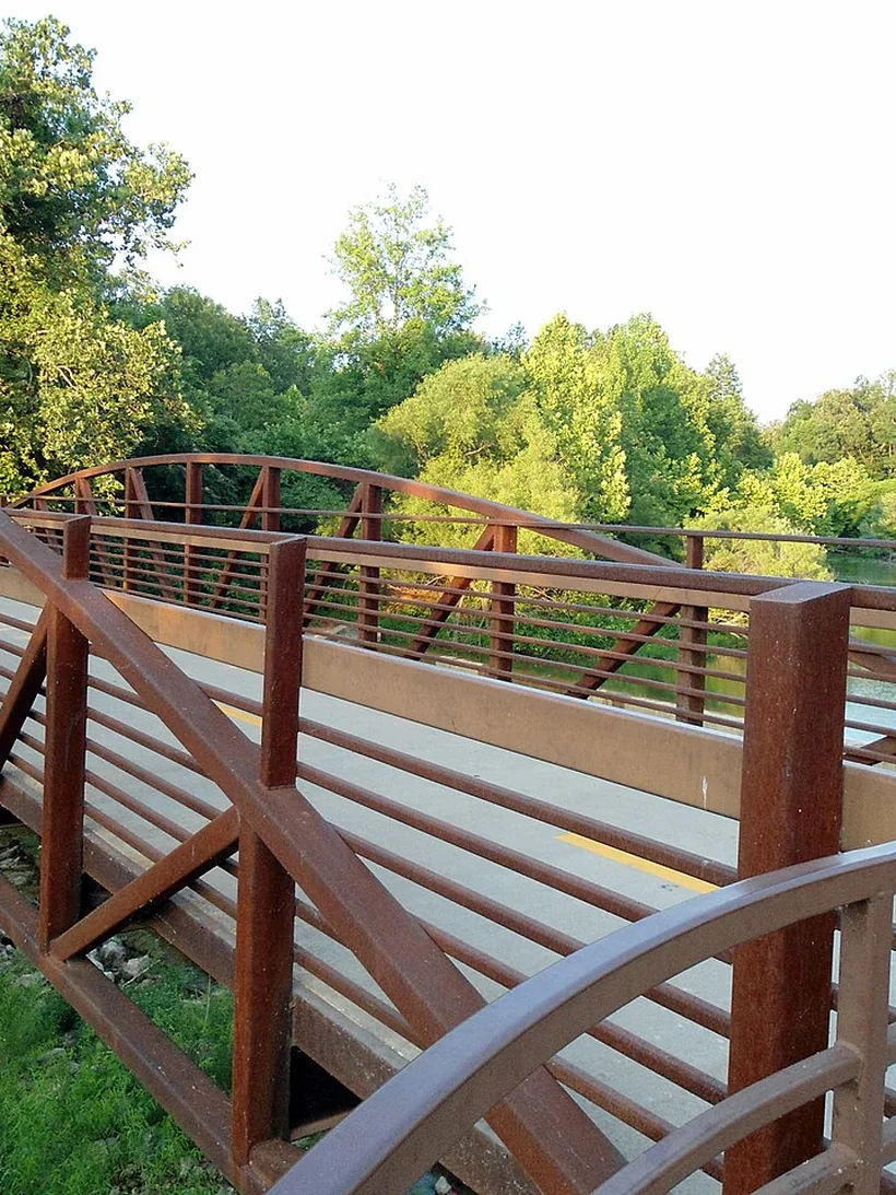A weathered steel trail bridge on the Razorback Greenway crossing Lake Fayetteville